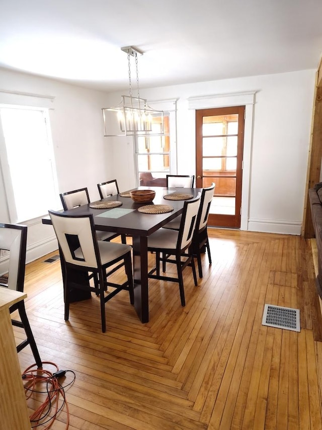 dining space with a chandelier, light wood finished floors, visible vents, and baseboards