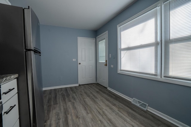 interior space featuring visible vents, baseboards, dark wood-style flooring, freestanding refrigerator, and white cabinetry