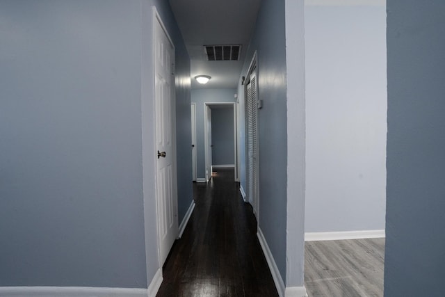 corridor with a barn door, wood finished floors, visible vents, and baseboards