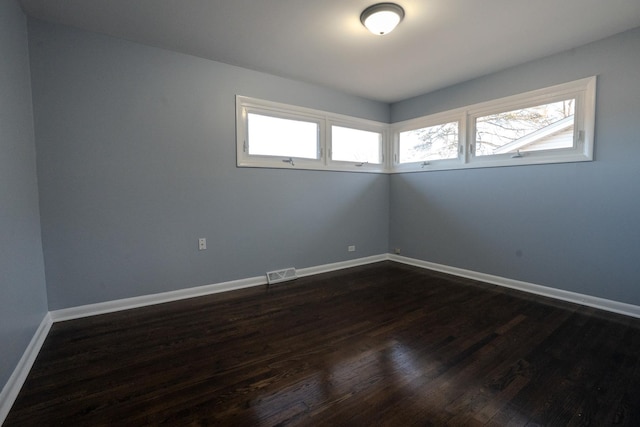 empty room with dark wood-style flooring, visible vents, and baseboards