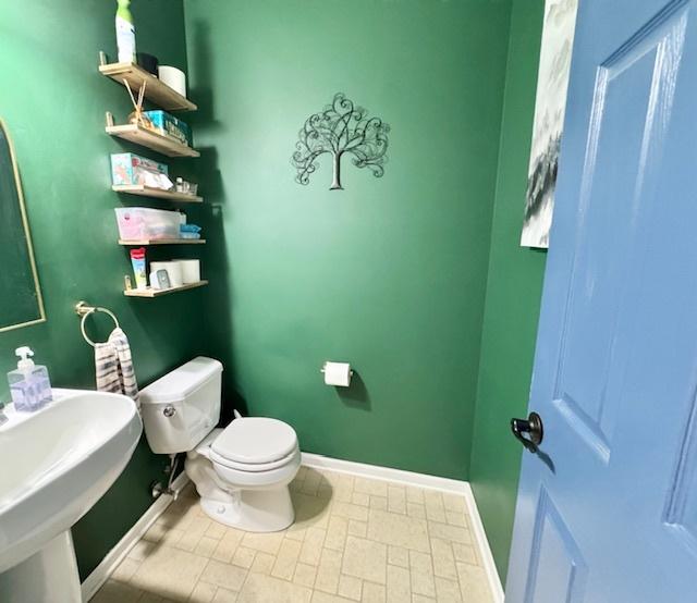 half bathroom featuring toilet, baseboards, and a sink