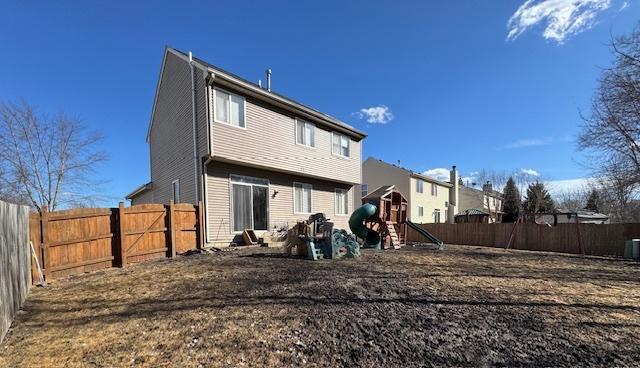 rear view of property featuring central air condition unit, a fenced backyard, and a playground