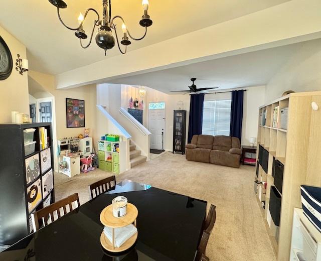 carpeted dining space with stairs, beam ceiling, and ceiling fan with notable chandelier