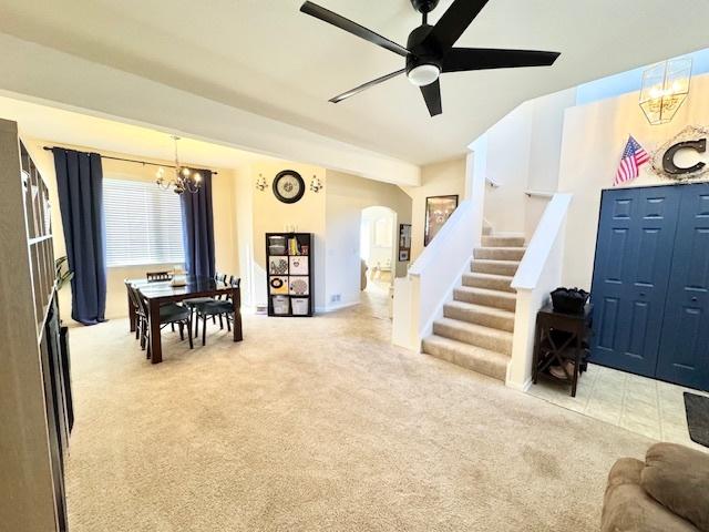 interior space featuring carpet floors, arched walkways, stairway, and ceiling fan with notable chandelier