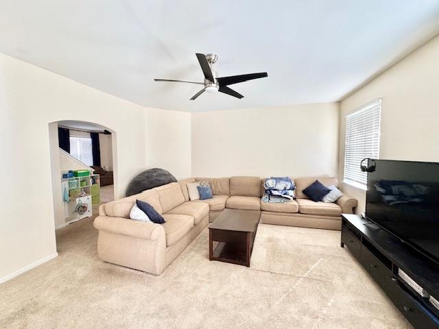 carpeted living room featuring a ceiling fan, arched walkways, a healthy amount of sunlight, and baseboards