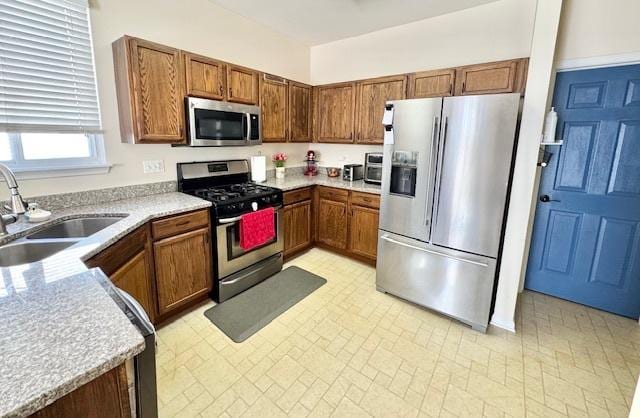 kitchen with brown cabinetry, stainless steel appliances, a sink, and light countertops