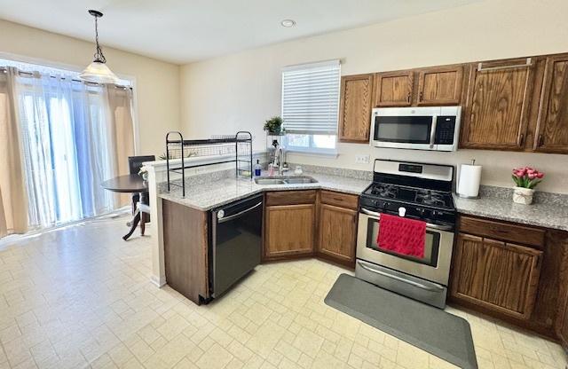 kitchen featuring stainless steel appliances, light countertops, a sink, and a peninsula