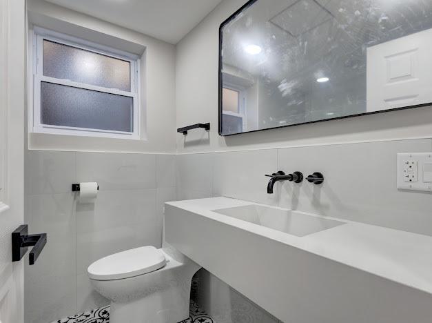 bathroom featuring a sink, toilet, and tile walls