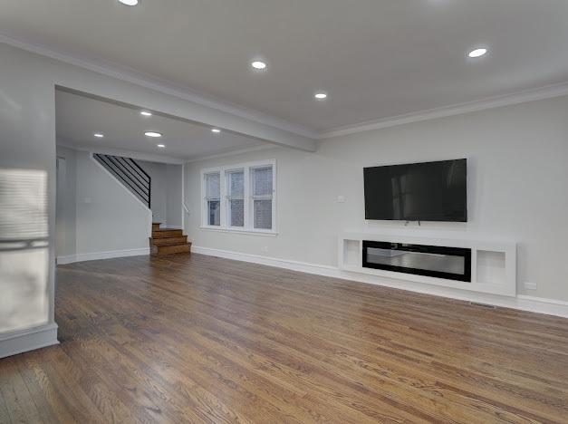 unfurnished living room featuring ornamental molding, a glass covered fireplace, stairway, and wood finished floors