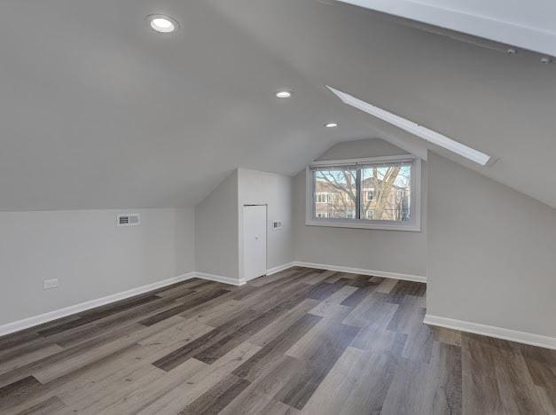 additional living space featuring vaulted ceiling with skylight, visible vents, baseboards, and wood finished floors