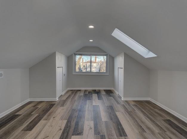 additional living space with lofted ceiling with skylight, baseboards, wood finished floors, and recessed lighting