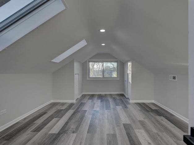 bonus room featuring lofted ceiling with skylight, recessed lighting, wood finished floors, and baseboards