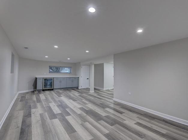 unfurnished living room featuring beverage cooler, light wood-type flooring, and baseboards