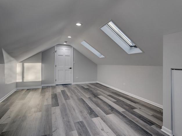 additional living space featuring lofted ceiling with skylight, wood finished floors, and baseboards