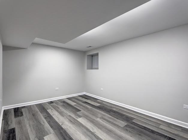 spare room featuring baseboards and dark wood-type flooring