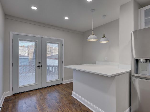 kitchen with a peninsula, dark wood-type flooring, baseboards, french doors, and pendant lighting