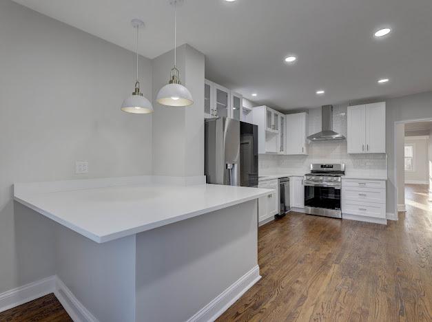 kitchen featuring wall chimney exhaust hood, glass insert cabinets, appliances with stainless steel finishes, dark wood-style flooring, and white cabinetry