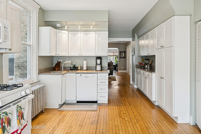 kitchen with white appliances, white cabinets, radiator heating unit, light wood-style flooring, and a sink