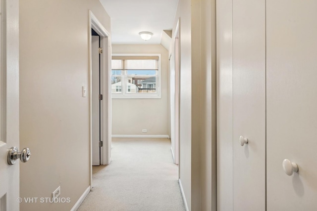 hallway with baseboards and light colored carpet