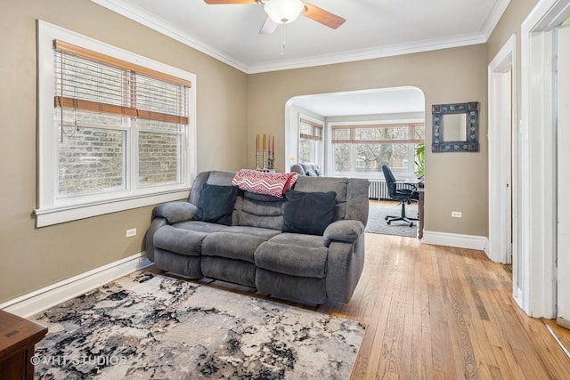 living room featuring light wood-style floors, baseboards, ornamental molding, and a ceiling fan