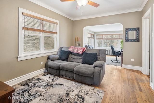 living area with light wood finished floors, a ceiling fan, baseboards, and crown molding