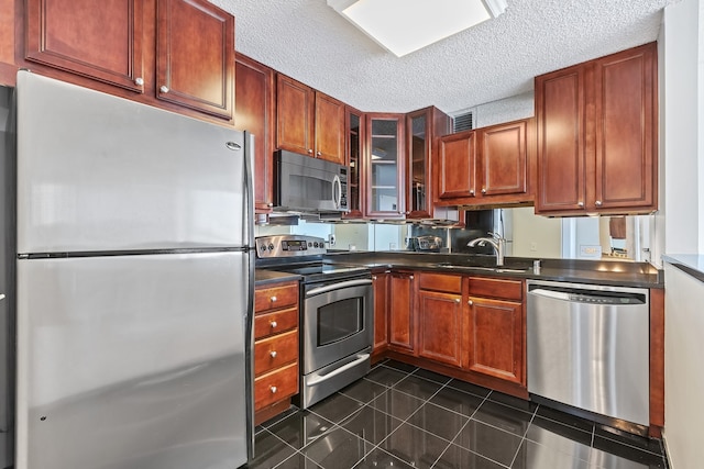 kitchen with dark tile patterned floors, dark countertops, a textured ceiling, stainless steel appliances, and glass insert cabinets