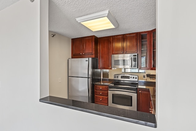 kitchen with stainless steel appliances, dark brown cabinets, glass insert cabinets, a textured ceiling, and dark countertops