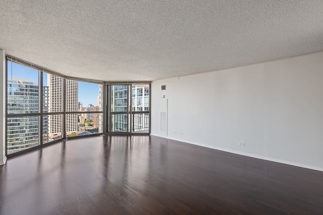 unfurnished room with expansive windows, wood finished floors, baseboards, a textured ceiling, and a city view