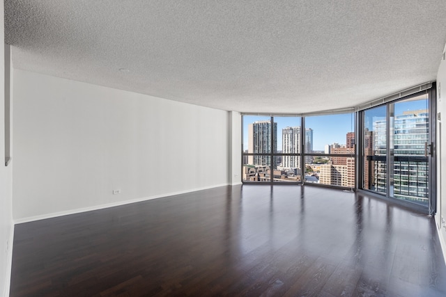 unfurnished room featuring a view of city, a wall of windows, baseboards, and wood finished floors