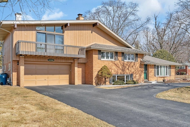 tri-level home with brick siding, a chimney, a balcony, a garage, and driveway