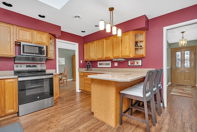 kitchen featuring stainless steel appliances, glass insert cabinets, light wood-style floors, and a breakfast bar area