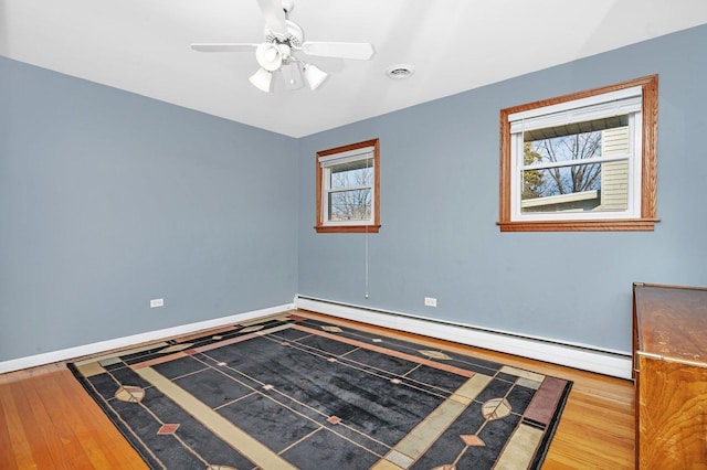 spare room featuring a wealth of natural light, baseboard heating, wood finished floors, and visible vents