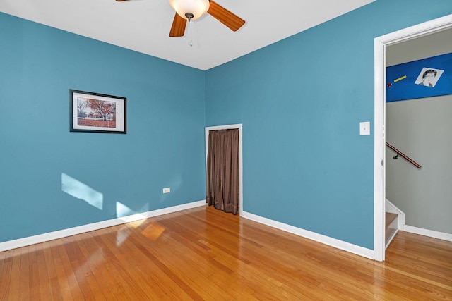 spare room with ceiling fan, stairway, wood-type flooring, and baseboards