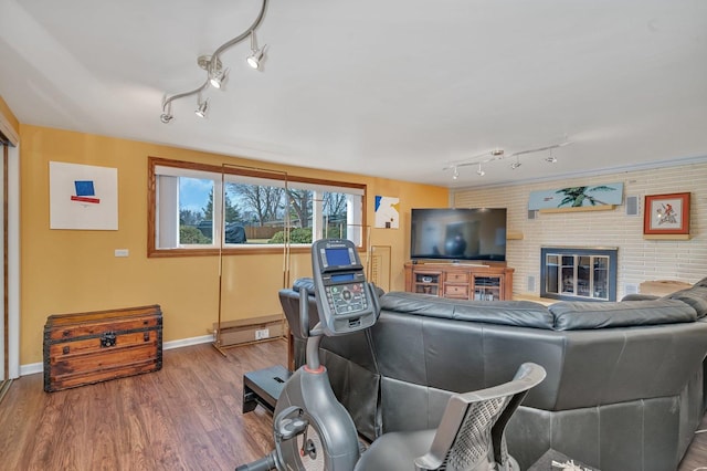 living area featuring an accent wall, a brick fireplace, brick wall, wood finished floors, and baseboards