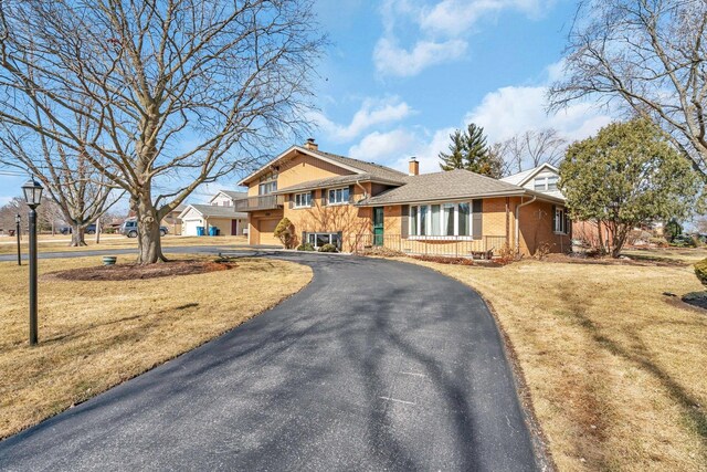 split level home with a front yard, brick siding, driveway, and a chimney