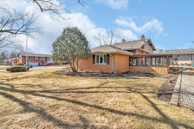 view of home's exterior with a lawn, brick siding, a chimney, and a sunroom