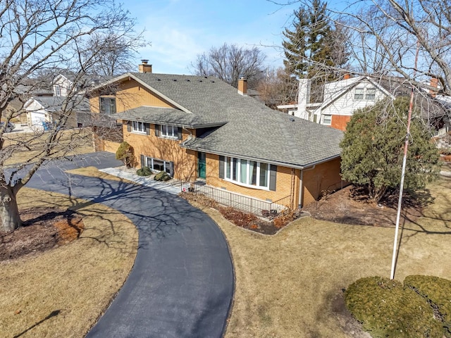 tri-level home featuring driveway, a shingled roof, a chimney, and brick siding