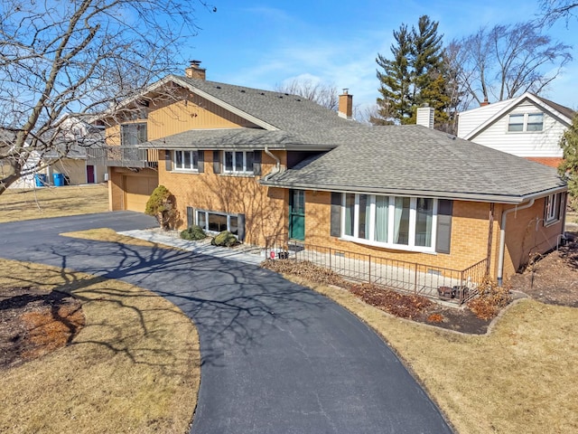 tri-level home with brick siding, driveway, a chimney, and roof with shingles