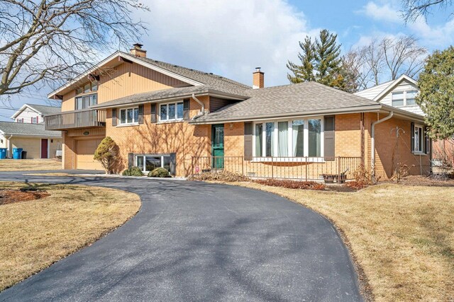 tri-level home featuring driveway, roof with shingles, a chimney, and brick siding