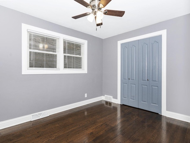 unfurnished bedroom with a closet, dark wood finished floors, visible vents, and baseboards