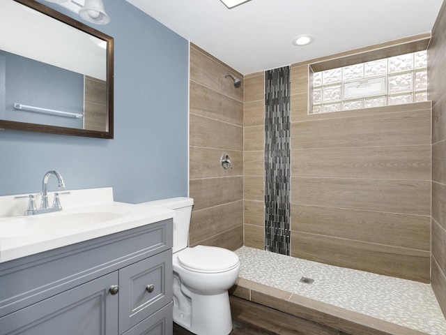 full bath with vanity, a tile shower, and toilet