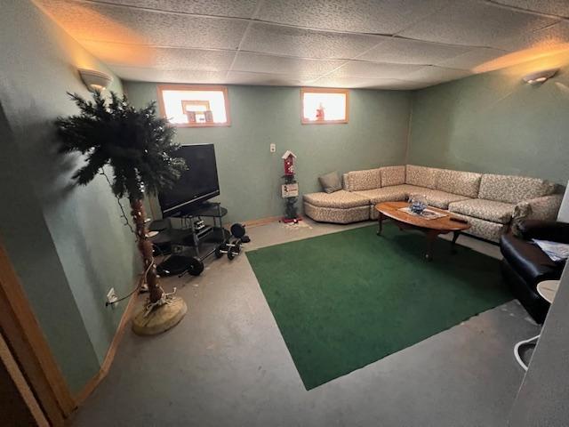 living room with concrete flooring, a drop ceiling, and baseboards