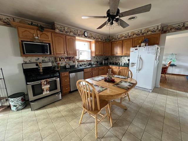 kitchen with appliances with stainless steel finishes, dark countertops, a sink, and brown cabinets