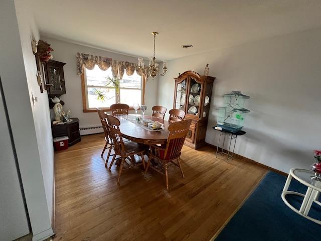 dining area featuring baseboards, a baseboard radiator, wood finished floors, and a notable chandelier