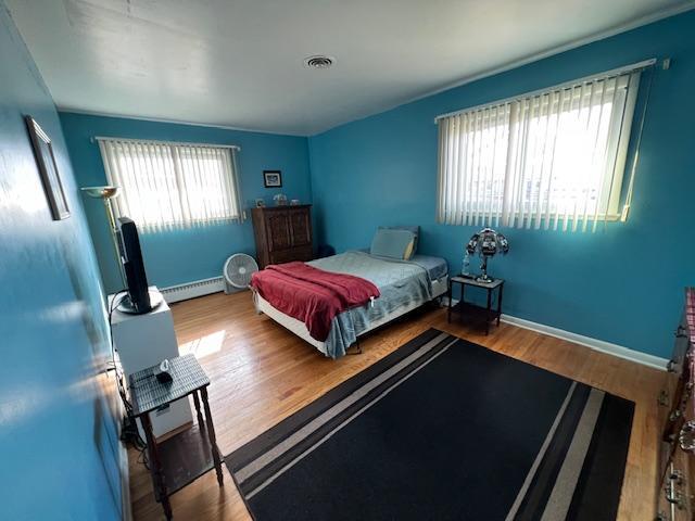 bedroom with baseboards, visible vents, baseboard heating, and wood finished floors