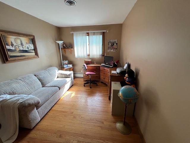 office space with light wood-style flooring, a baseboard radiator, and visible vents