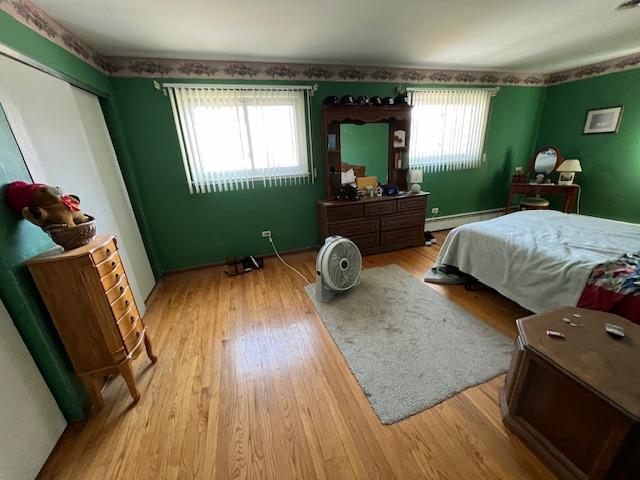 bedroom with multiple windows, a baseboard heating unit, and wood finished floors