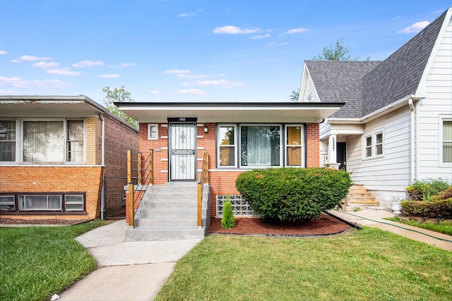 view of front of house featuring a shingled roof, a front yard, and brick siding