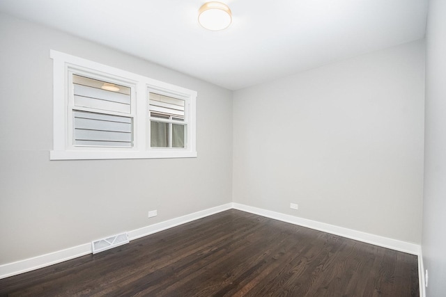 empty room featuring dark wood-style flooring, visible vents, and baseboards