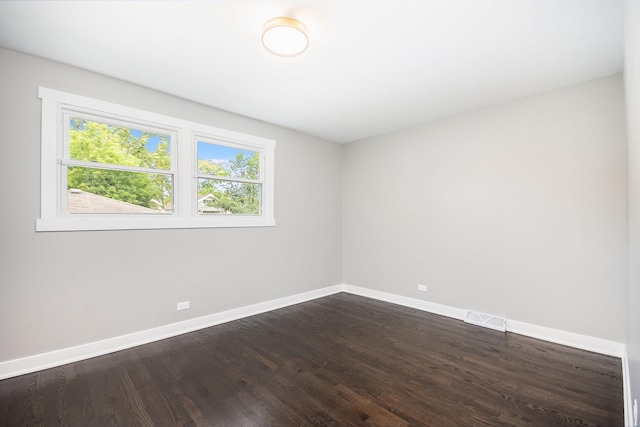 empty room featuring visible vents, dark wood finished floors, and baseboards